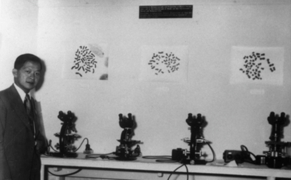 Black and white photo of man standing next to row of microscopes